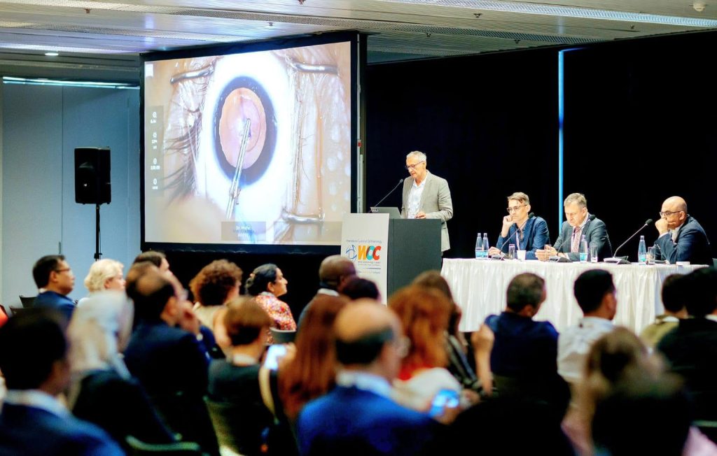 WOC 2026 conference session in Prague, with ophthalmologists presenting a live surgical procedure to an audience.
