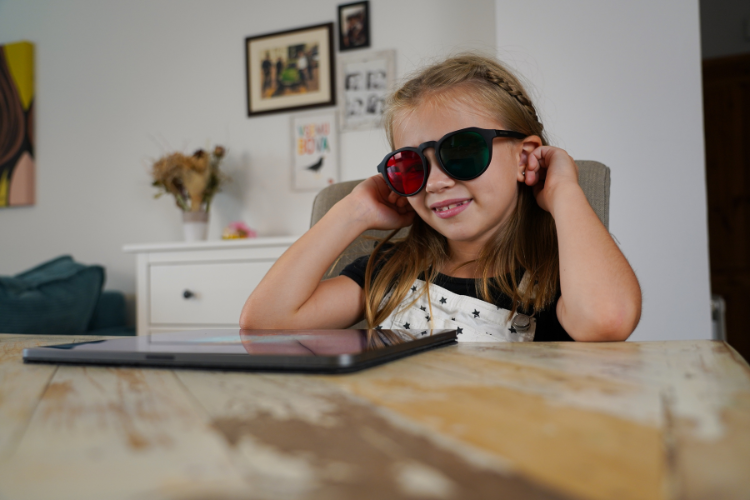 Child wearing red-green glasses while using a tablet during a vision training activity at home